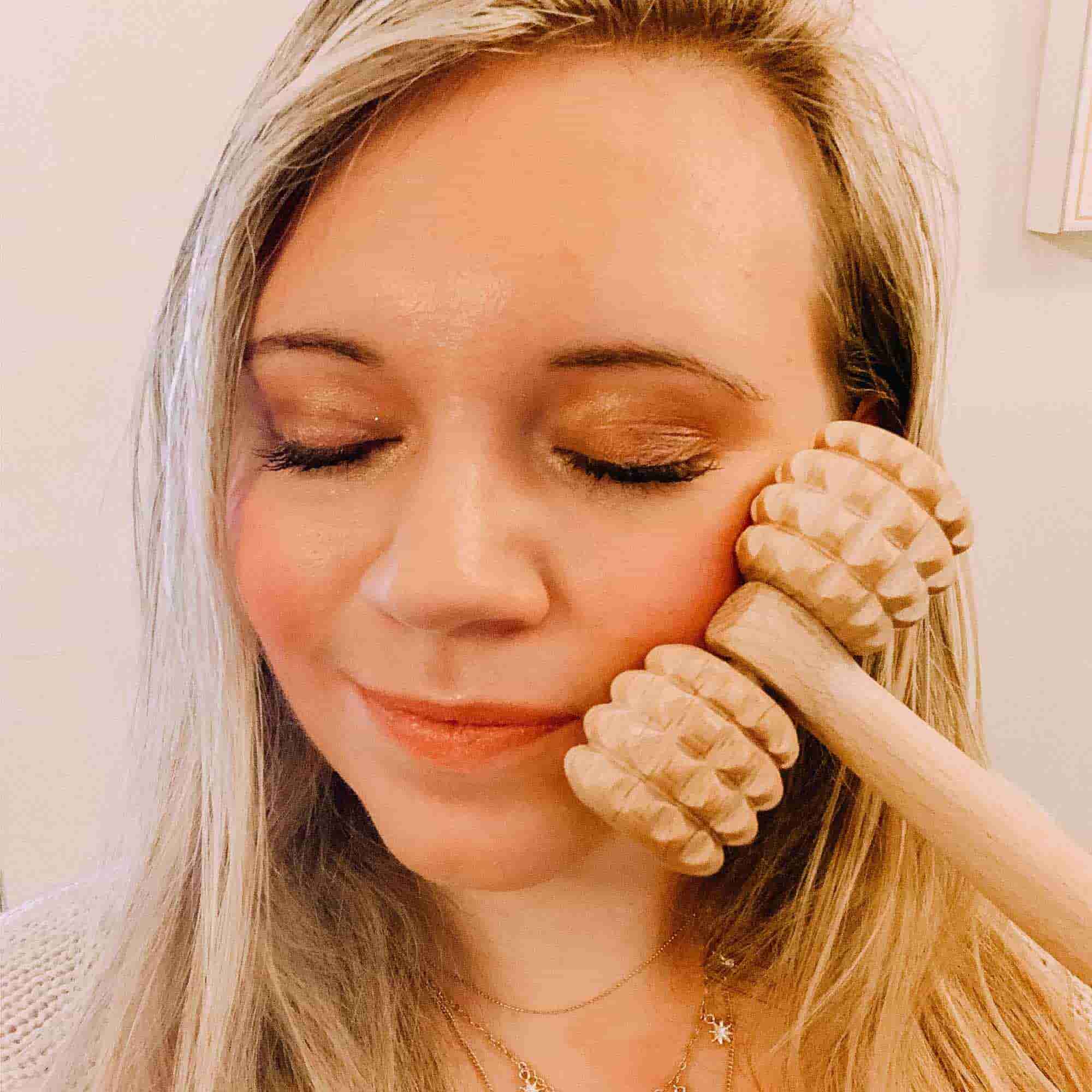 Wooden face massage roller used gently on the cheek as part of a self-care routine