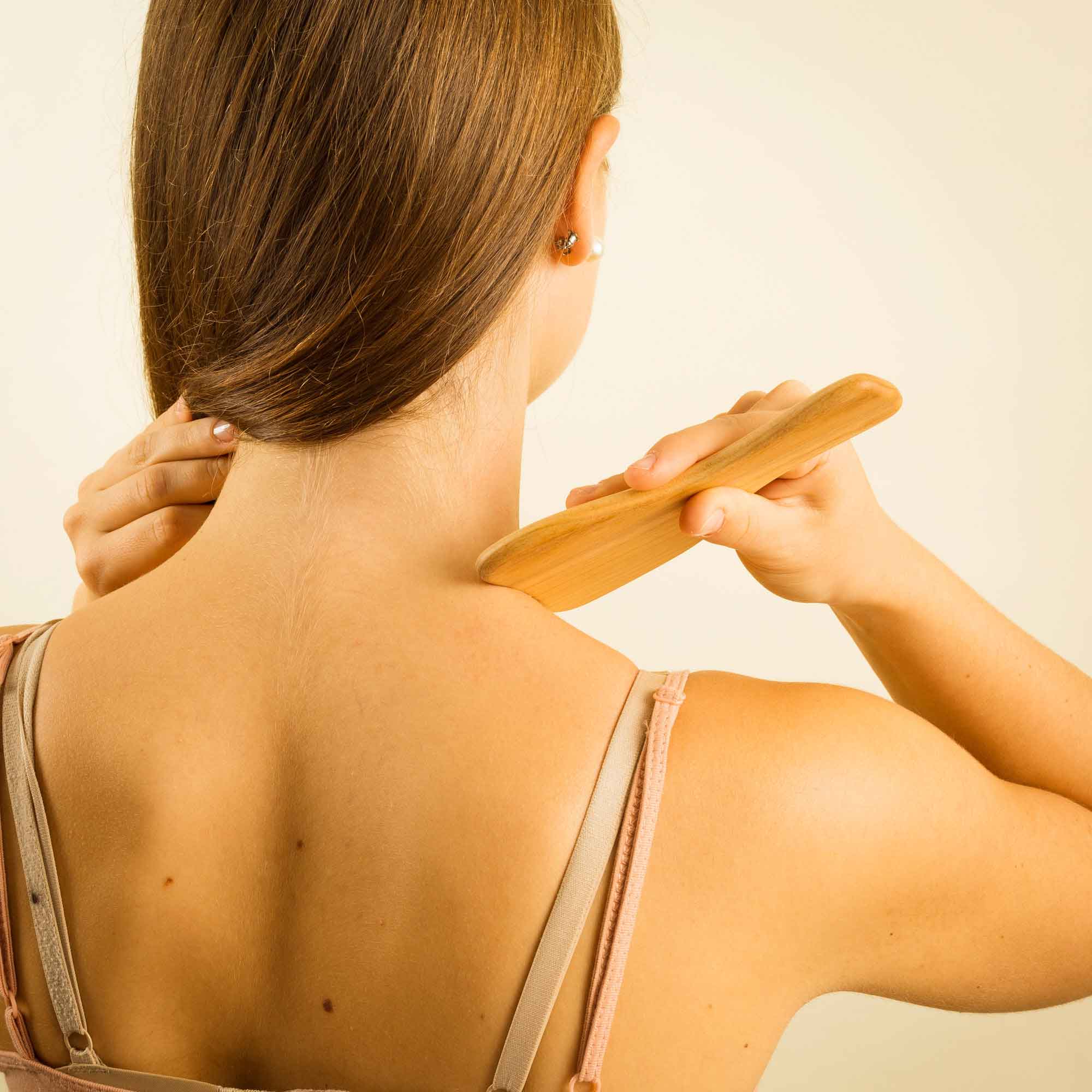 Wooden massage tool used gently on the neck and shoulder as part of a self-care routine