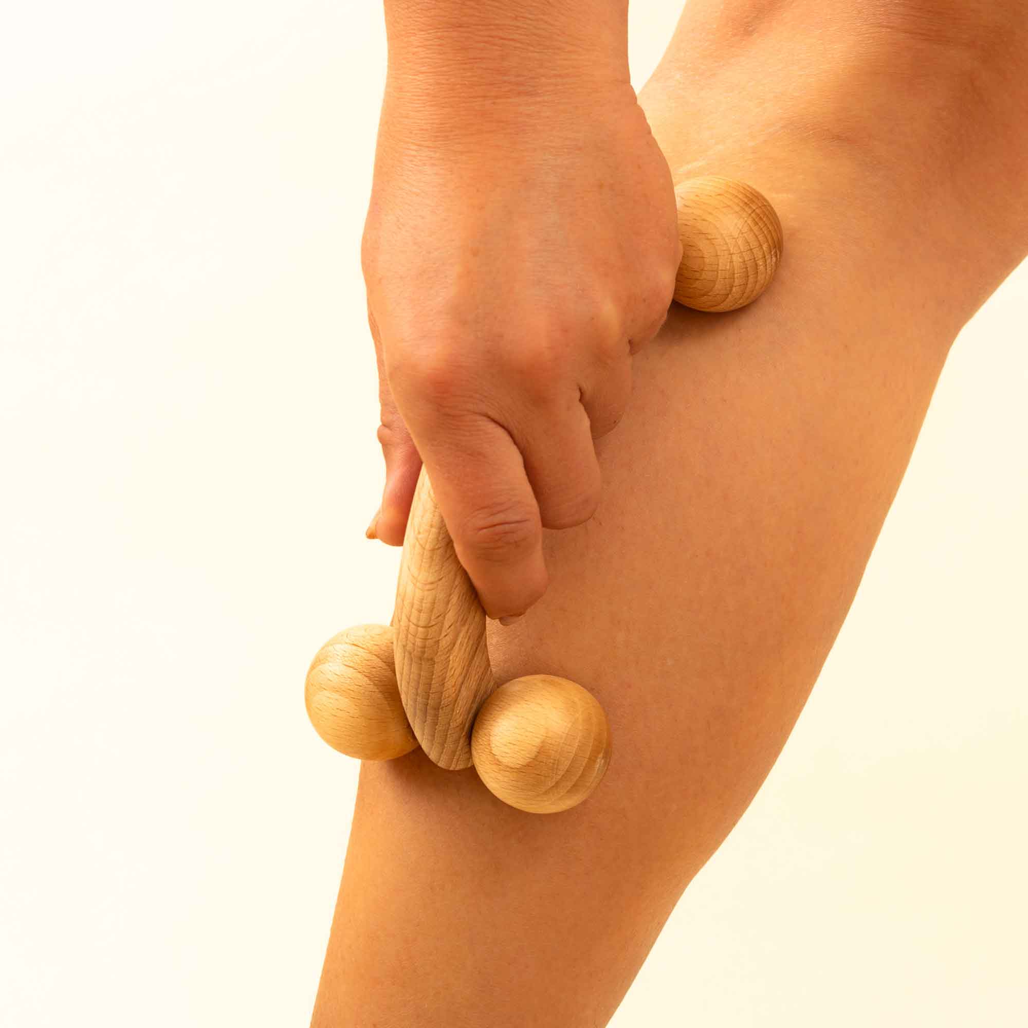Wooden handheld massage tool used gently on the leg as part of a home self-care routine