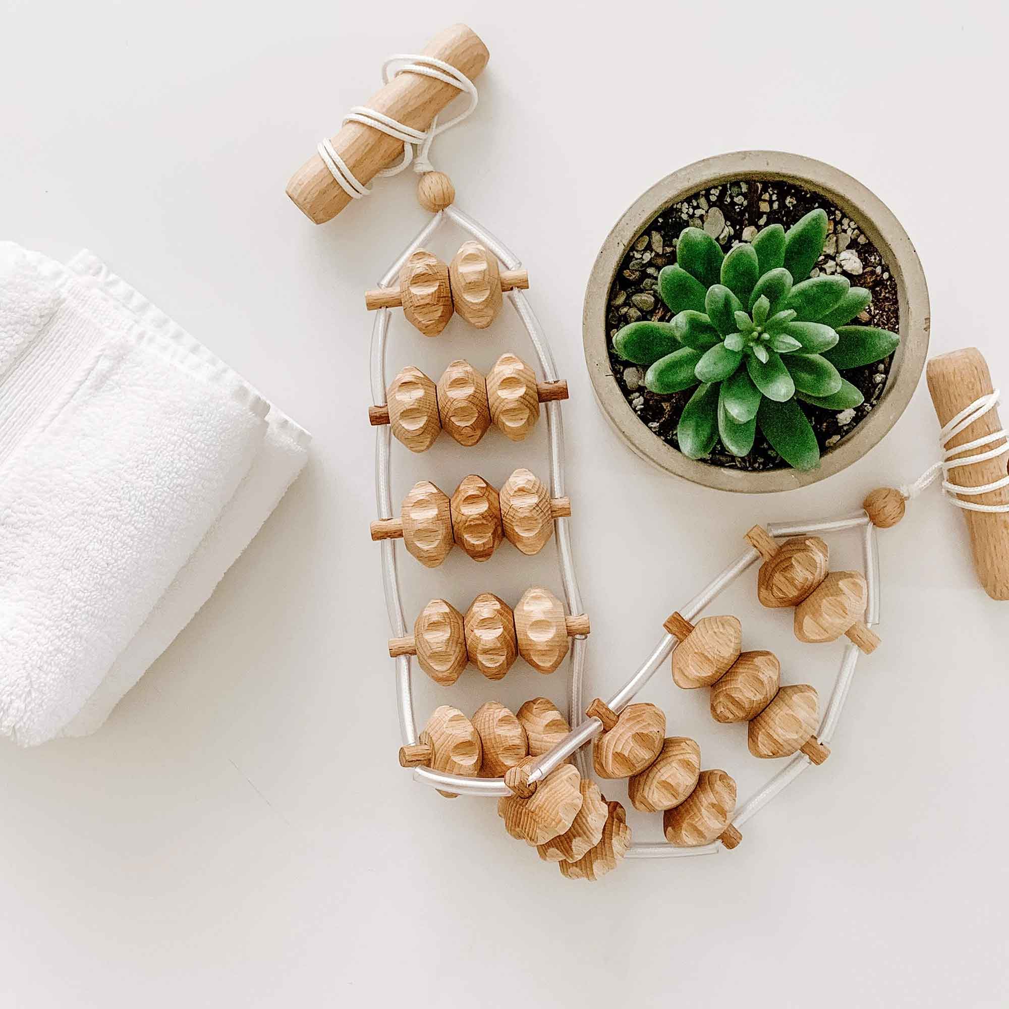 Wooden massage tools arranged with a towel and plant for a calm home self-care routine