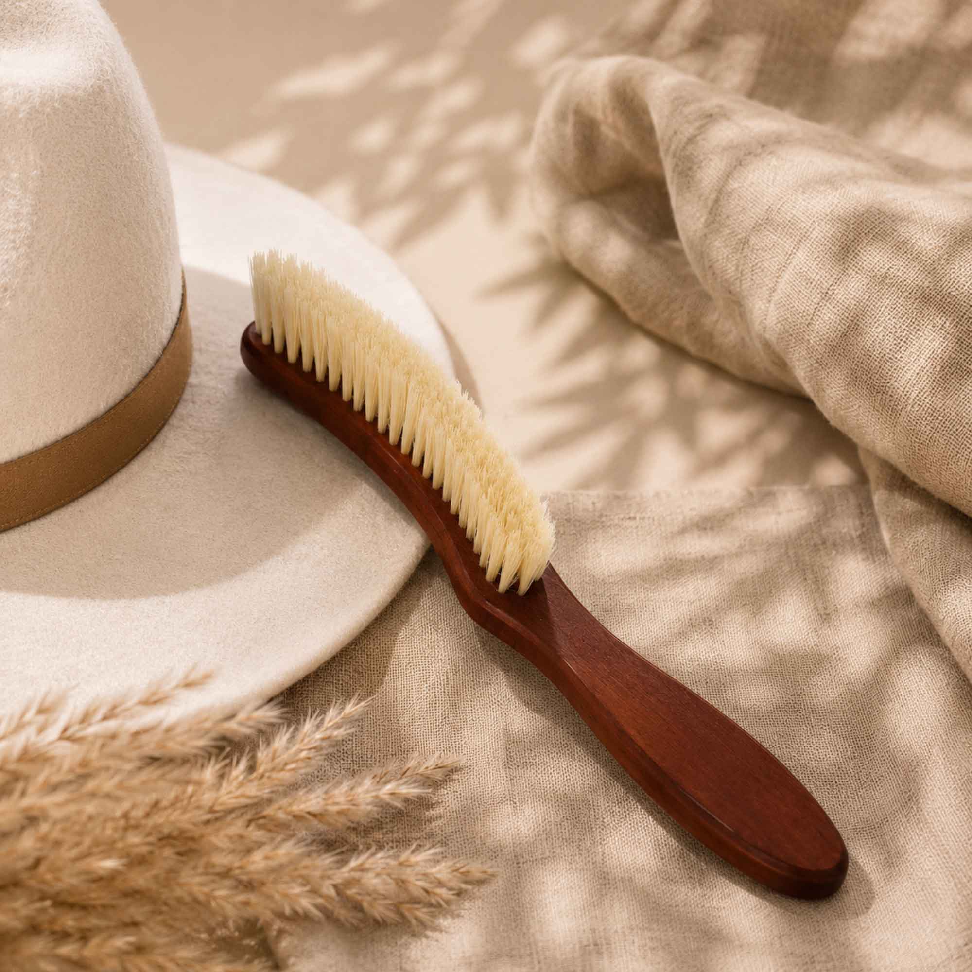Pear wood clothing brush displayed next to a light-colored hat on beige fabric