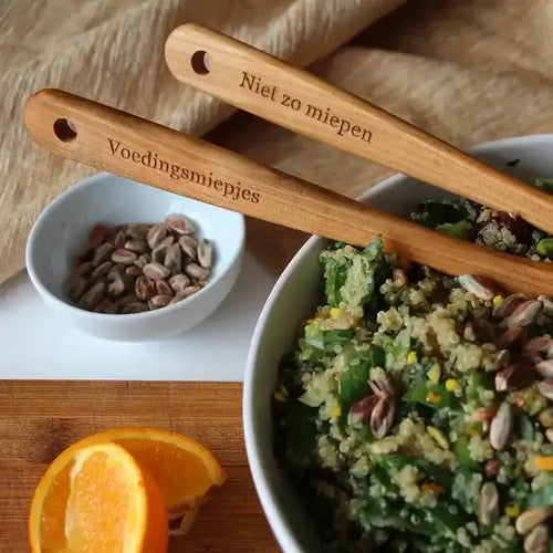 Personalised wooden spoons with engraved text placed beside a salad bowl