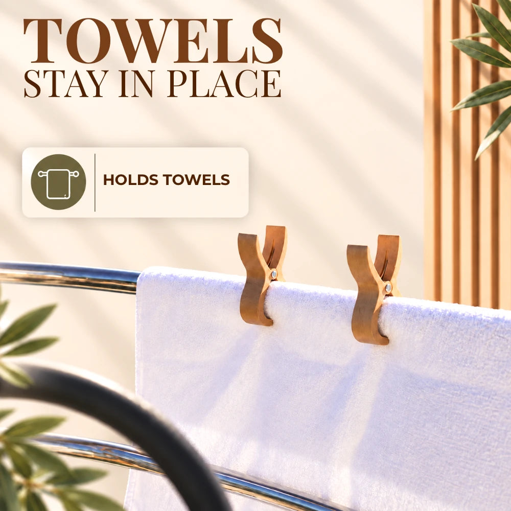 A white towel draped over a chrome bar, held in place by two tan clip-on towel holders. Large text at the top reads 'TOWELS STAY IN PLACE' with a badge that says 'HOLDS TOWELS'.