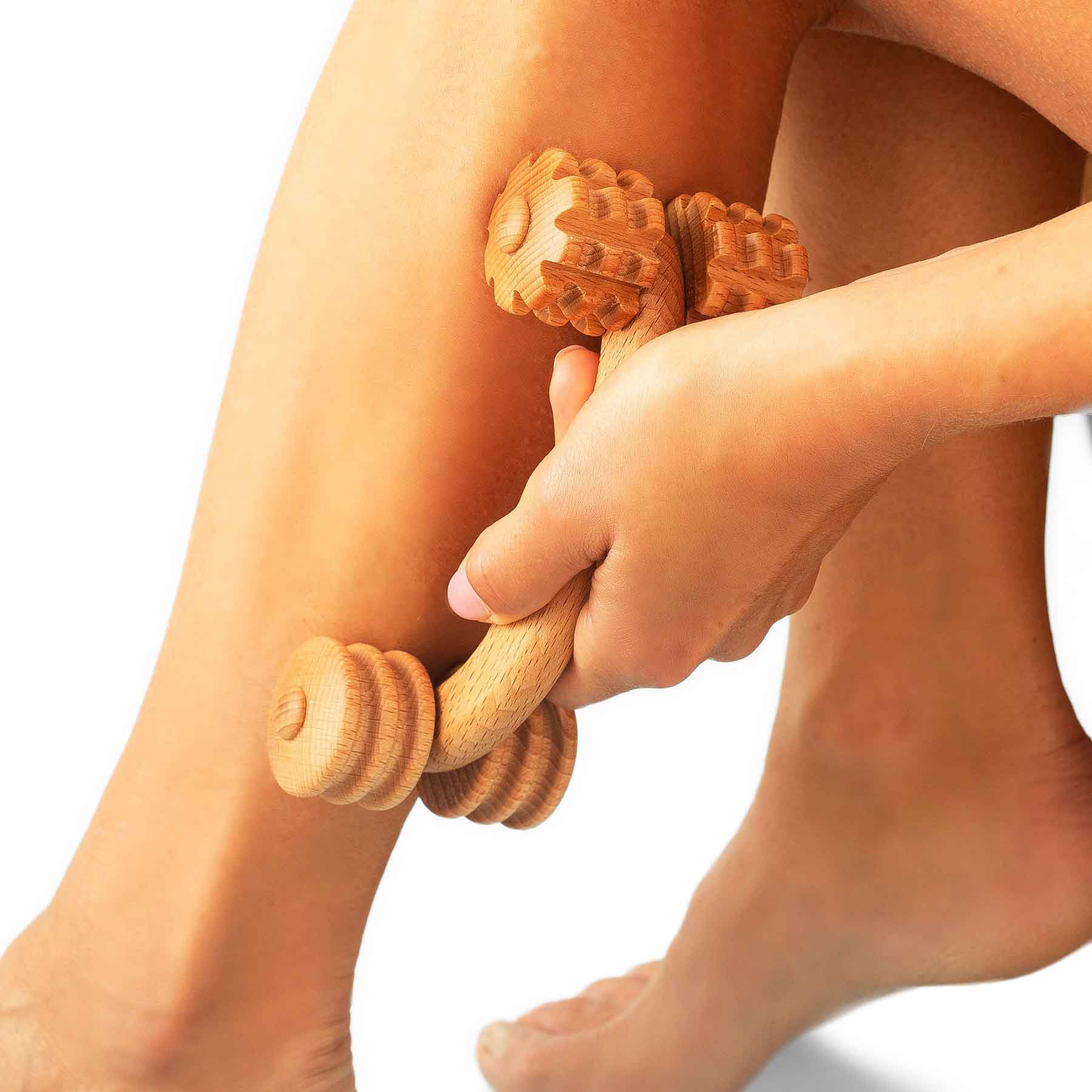 Person using a wooden massage roller on their leg against a white background