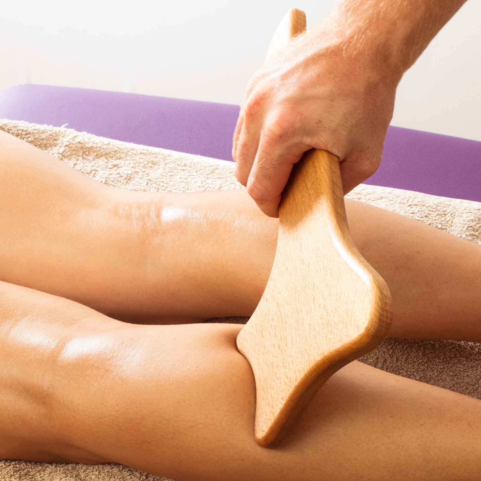 Hand using a wooden gua sha massage tool on the leg
