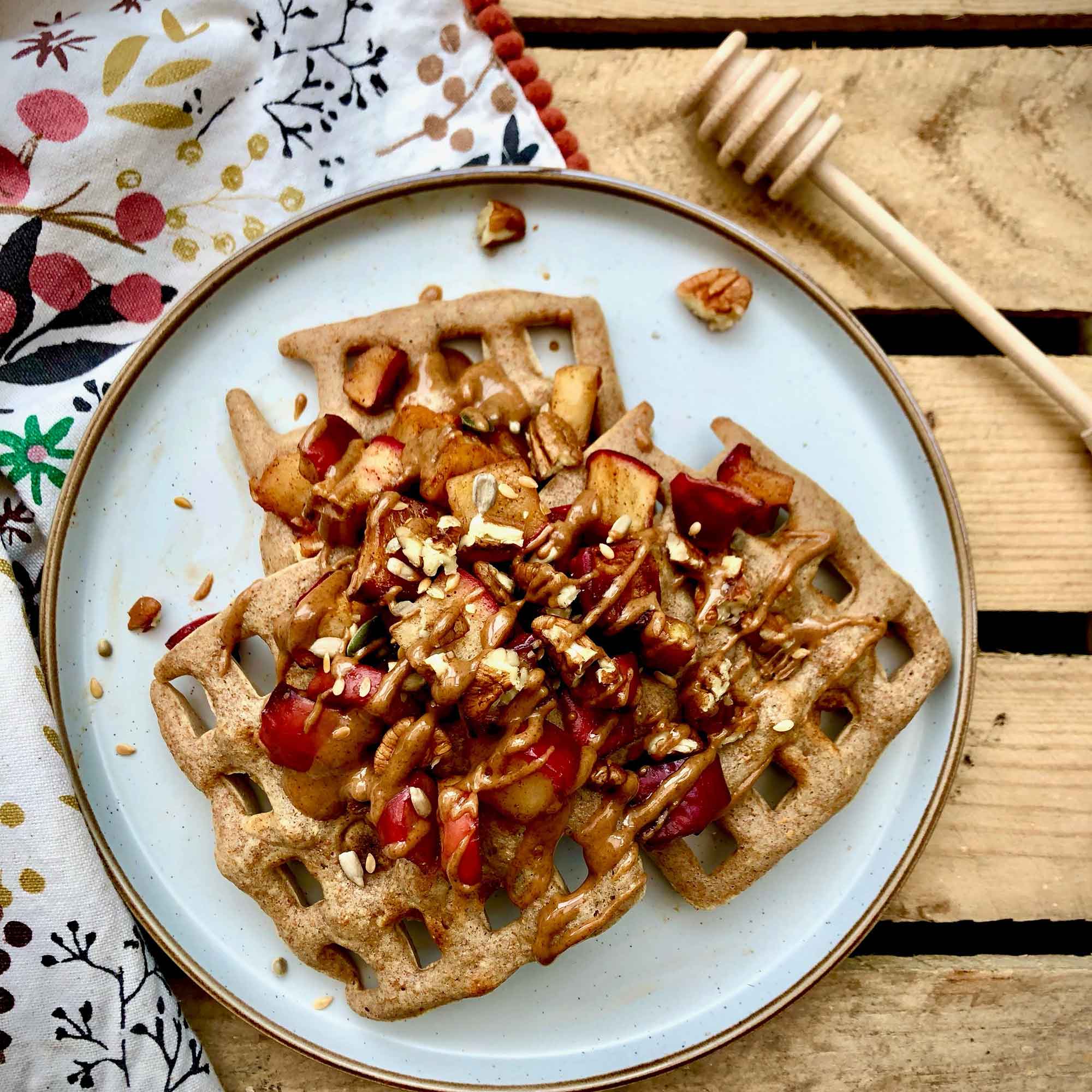 Wooden honey dipper beside breakfast waffles with fruit and nuts