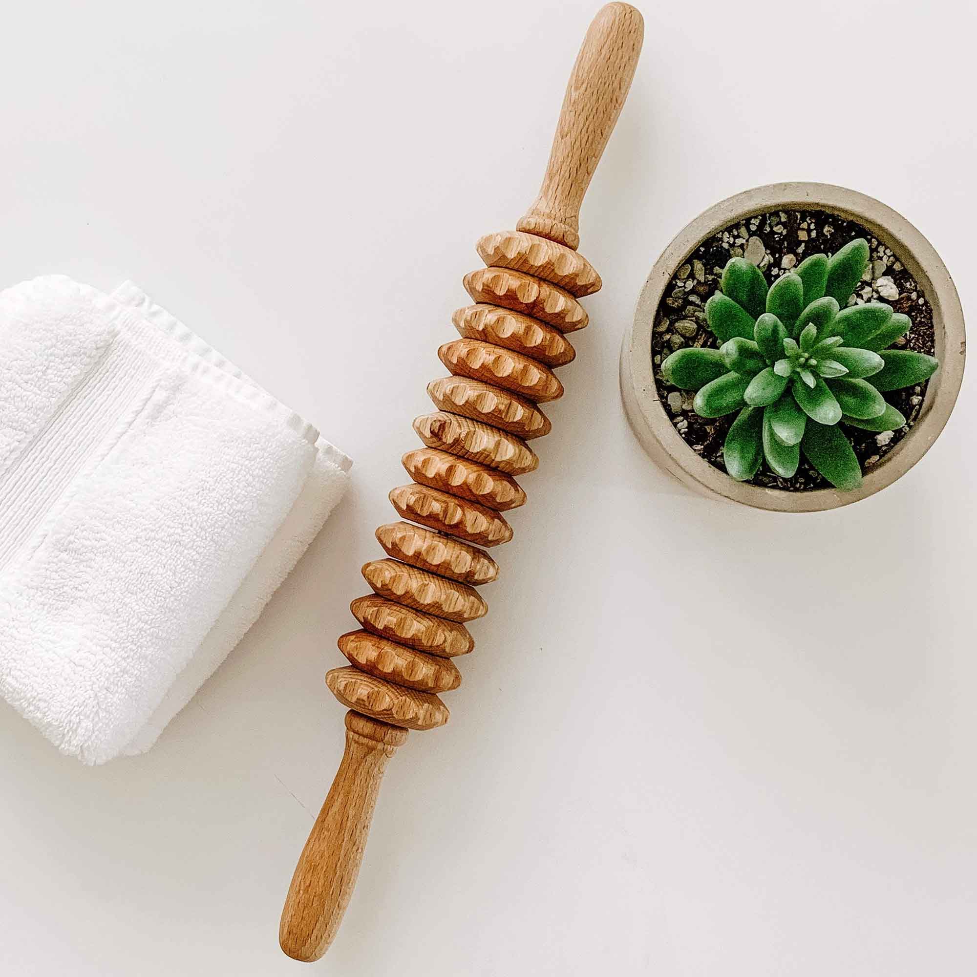 Wooden massage roller beside a towel and plant for a simple self-care routine