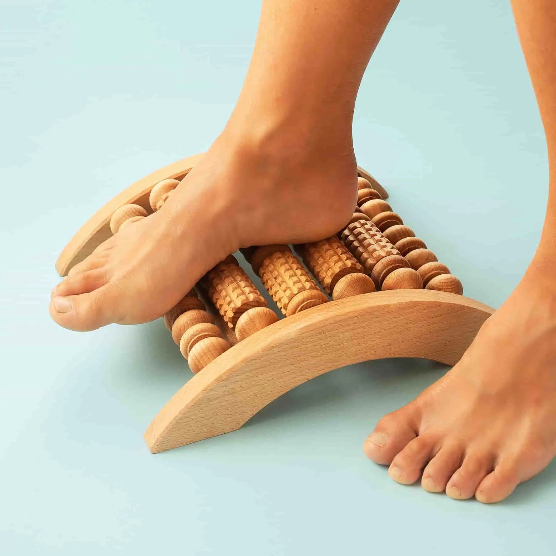 Bare feet using a wooden foot massager roller on the floor