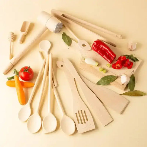 Wooden kitchen utensils arranged with vegetables and herbs on a light surface