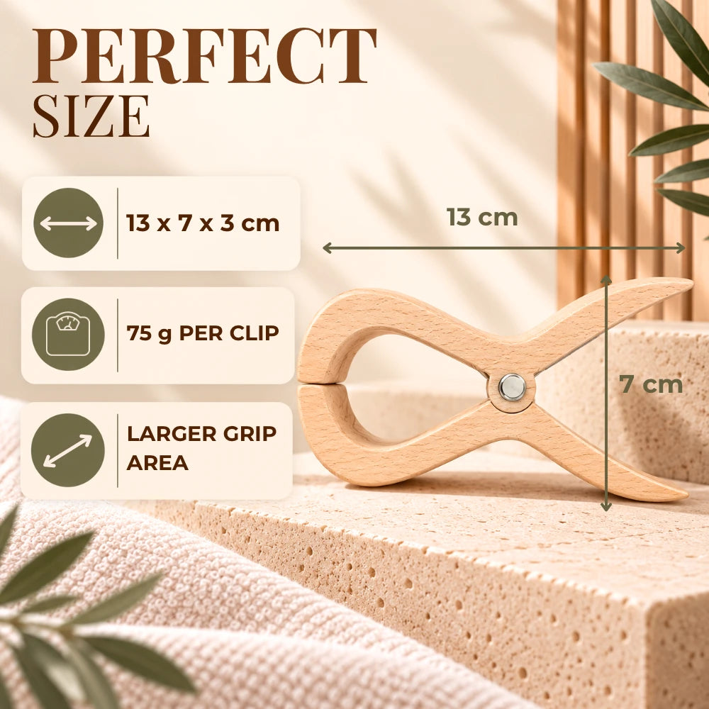 A wooden clothes clip shown on a beige textured surface with overlaid dimension arrows and text reading 13 x 7 x 3 cm, 75 g per clip, and larger grip area. The scene is styled with soft neutral props and a plant leaf, and the headline says PERFECT SIZE.